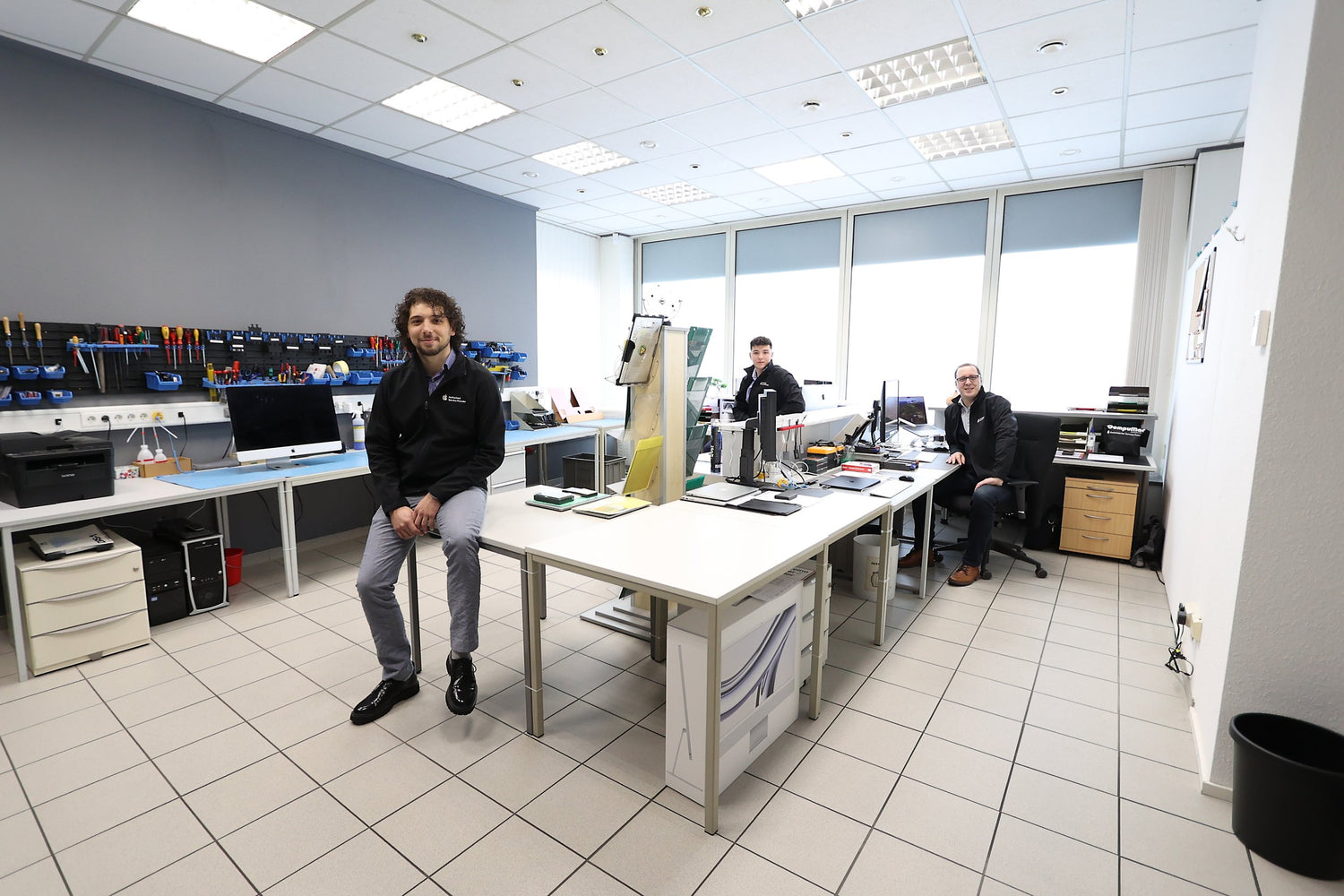 The CompuMac workshop: workbenches, a wall of tools, and three people from the team