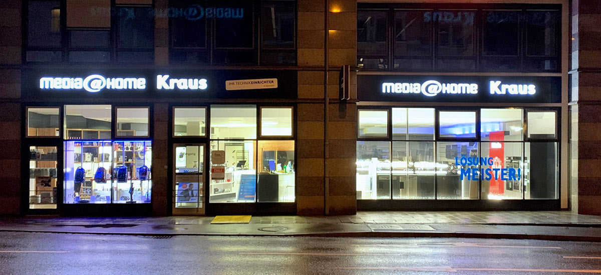 media@home Kraus in Kempten from the outside: lit shop windows and the sign above the entrance