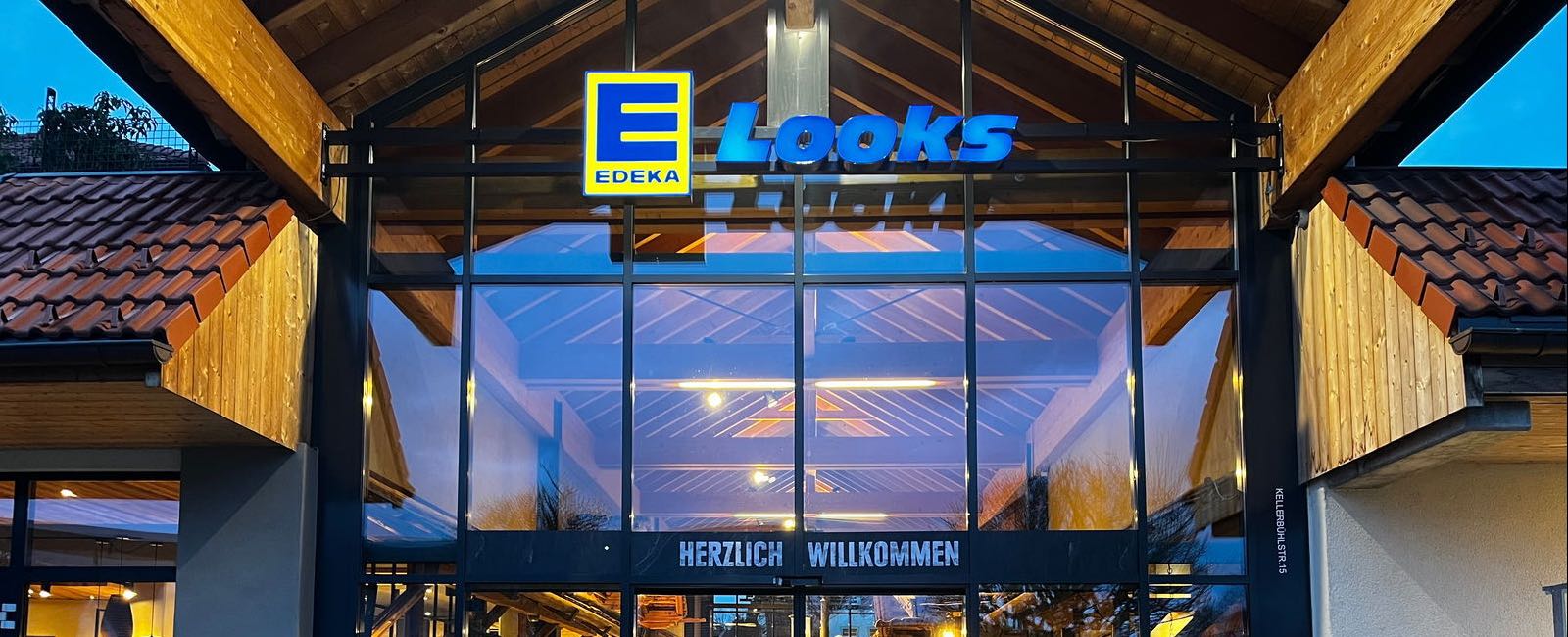 The entrance of EDEKA Looks in Neuravensburg: a glass front under a timber roof with the illuminated sign above