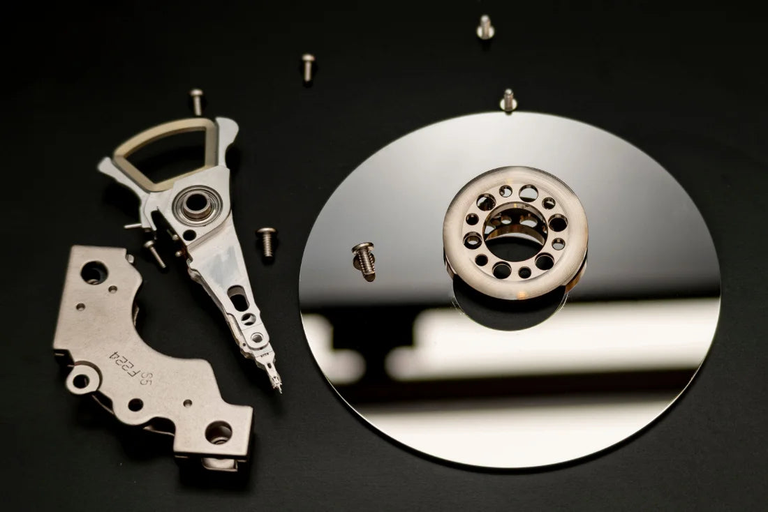 Hard drive parts on a black surface: platter, read/write arm, and screws