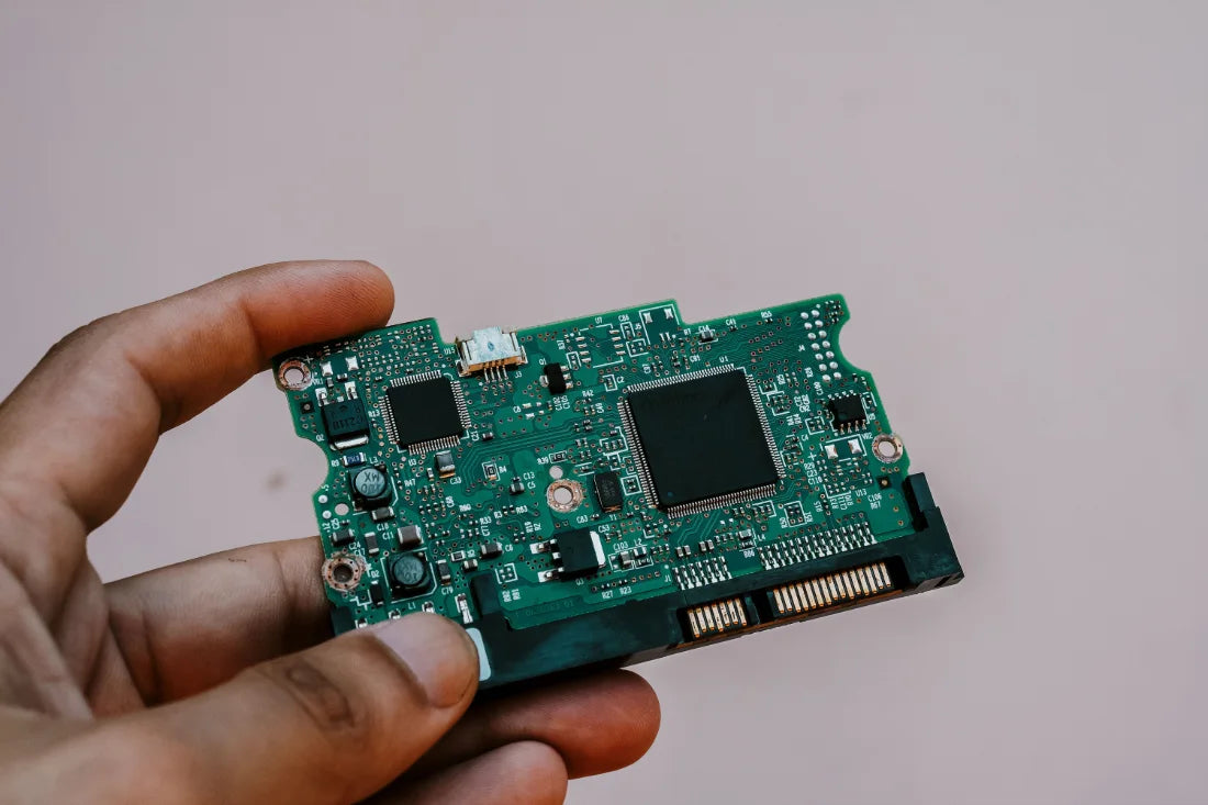 A hand holding the circuit board of a hard drive