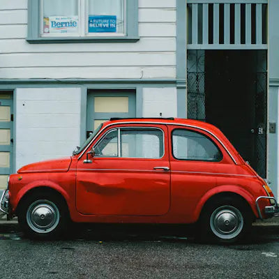 Small red classic car in front of a house