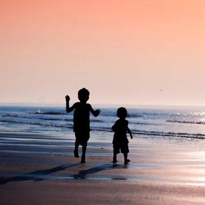 Two children in silhouette on a beach at sunset