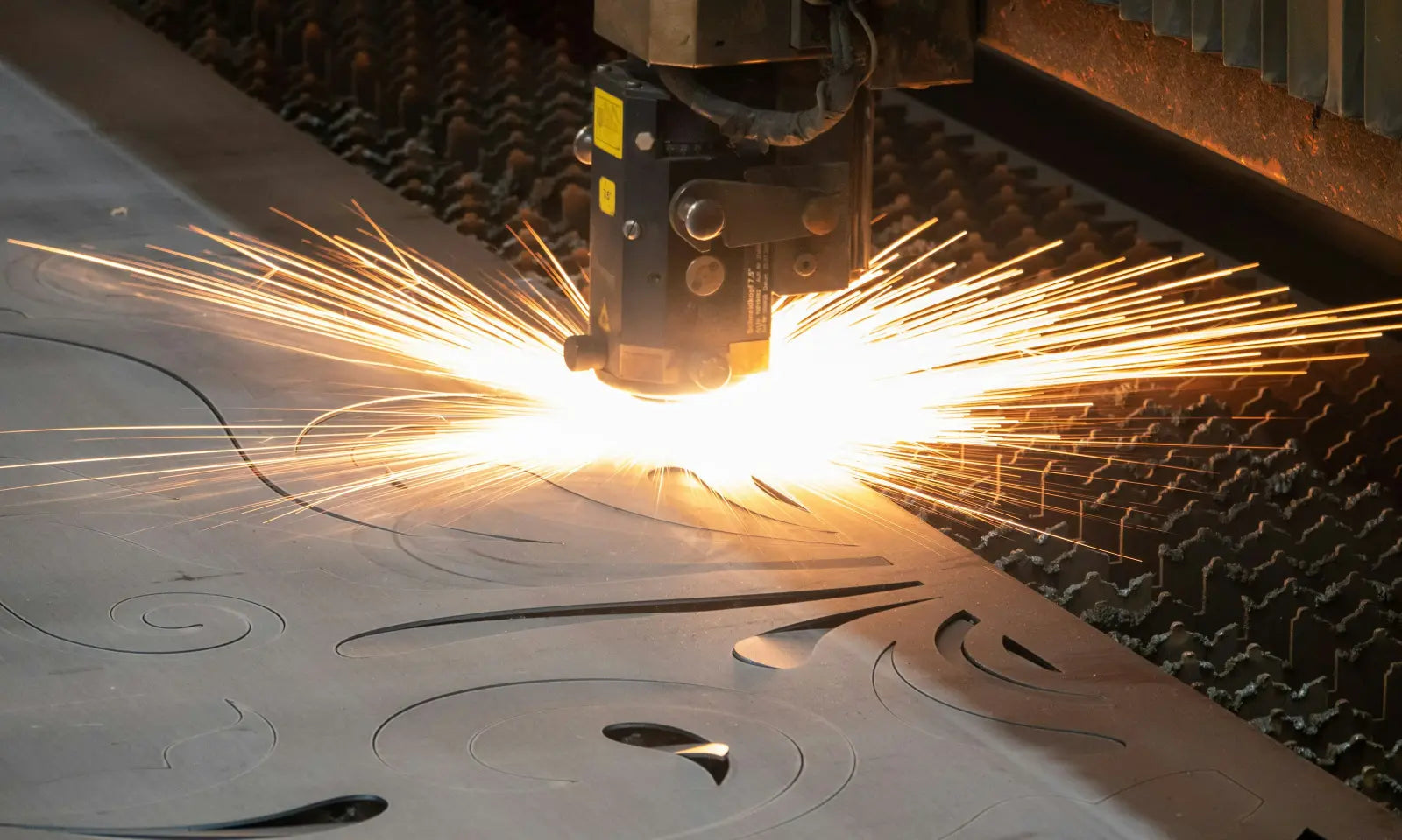 A cutting head works ornaments out of a steel sheet, with sparks spraying all around.
