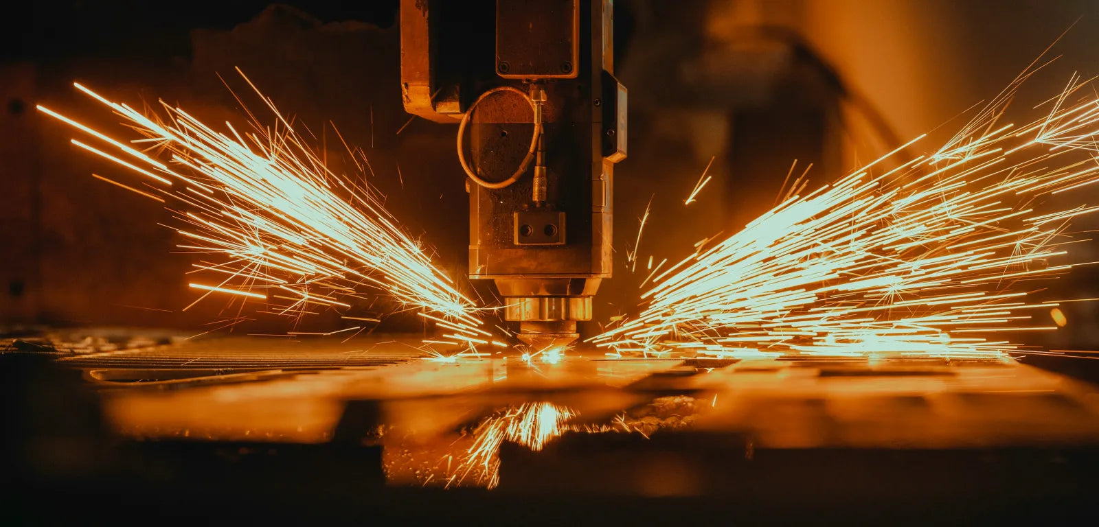 A machine head works on a metal plate, with bright sparks flying to both sides.