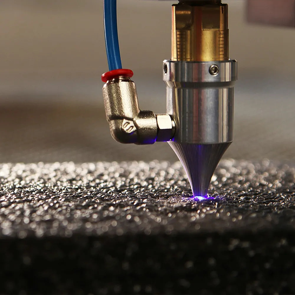 Close-up of a laser nozzle: a violet point of light glows at its tip on dark material.